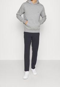 Felpa grigia con tasca frontale, maniche lunghe e cappuccio regolabile. Abbinata a pantaloni blu navy e sneakers bianche. Design semplice, texture morbida.