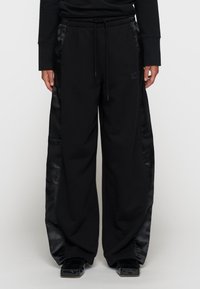 Zwarte sweatpants met satijnen zijpanelen, voorzien van een elastische tailleband, een trekkoord en een numeriek logo op de voorkant.