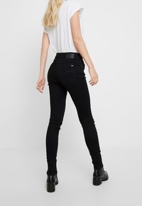 Vaqueros ajustados negros de cintura alta, con una textura suave y dos bolsillos traseros. Combinados con una camiseta blanca lisa y botines hasta el tobillo.