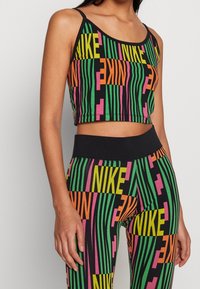 Czarny crop top i legginsy z wyrazistym, wielokolorowym napisem "NIKE" w zielonym, różowym i żółtym kolorze oraz pionowymi paskami. Elastyczny materiał.