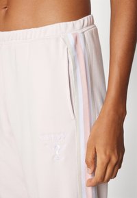 Lichtroze sweatpants met een tailleband met trekkoord, zijzakken en geborduurd "GUESS" logo. Beschikt over meerkleurige strepen langs de zijkanten.