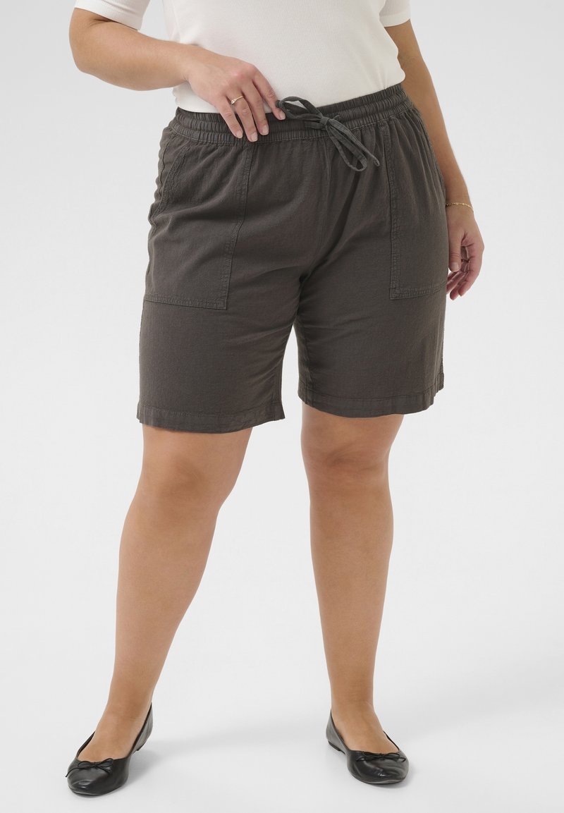 Personne portant un short gris foncé à cordon avec de grandes poches avant, des ballerines noires et un haut blanc à manches courtes.