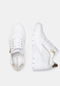White athletic shoes featuring mesh panels, gold accents, a side zipper, and a padded collar on a thick sole with a textured grip.