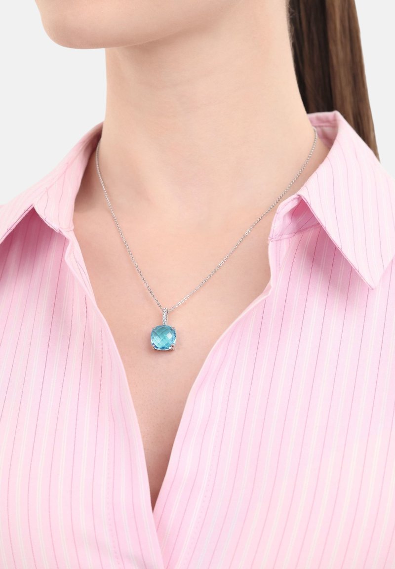 Collana d'argento con un pendente quadrato, di colore blu chiaro e sfaccettato. Indossata su una camicia a righe rosa con colletto, che mette in risalto la chiarezza e la forma del pendente.