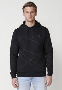 Hanorac negru cu un model geometric texturat. Are un glugă cu șnur și manșete cu elastic. Materialul pare moale și elastic.