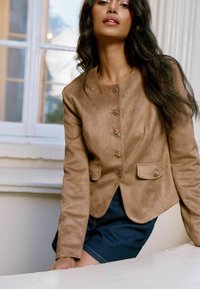 Veste en suède synthétique marron au design ajusté, col rond, boutons décoratifs et deux poches avant, assortie à un short en denim.