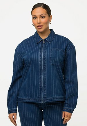 Giacca di denim blu scuro con una sottile striscia verticale bianca, zip frontale, colletto a punta e taschino sul petto. Maniche lunghe.