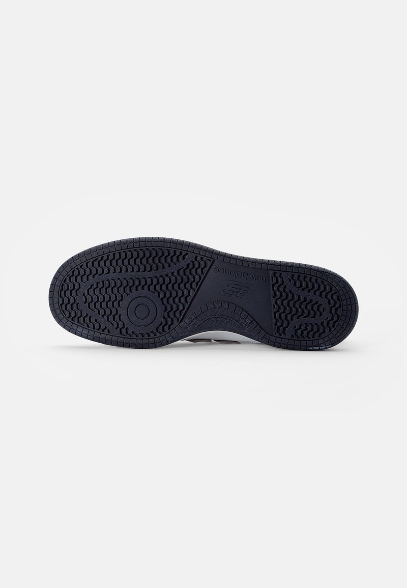 Semelle d'une sneaker avec une surface en caoutchouc noir texturé, présentant un motif de bande de roulement détaillé et un élément de design en forme de cercle.