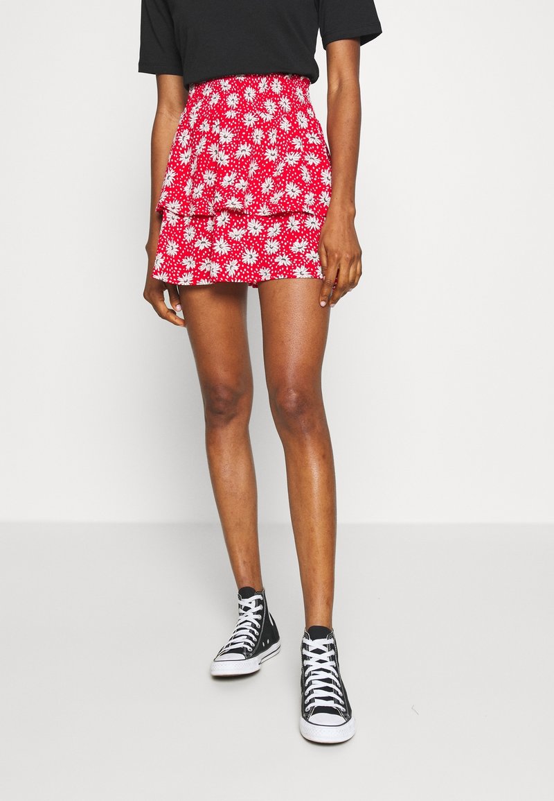 Gonna mini rossa a fiori con motivi a margherita bianchi, vita arricciata e design a strati con volant, abbinata a sneaker alte nere.