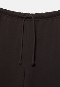 Pantaloni della tuta con elastico in vita nero e coulisse abbinata annodata con un semplice nodo al centro davanti.
