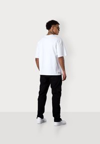 Weißes Baumwoll-T-Shirt mit einem lockeren Schnitt und kurzen Ärmeln, kombiniert mit schwarzen Cargo-Hosen und weißen Sneakers. Auffälliges Etikett auf dem Shirt.