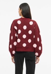 Suéter granate con grandes lunares rosas, mangas tipo globo y dobladillo acanalado. Fabricado con un tejido suave y texturizado, con un corte holgado.