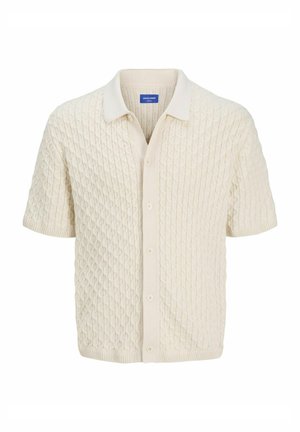 Polo shirt en tricot à manches courtes couleur crème, présentant un motif en losanges texturé, un devant boutonné et un col contrasté. Tissu doux.