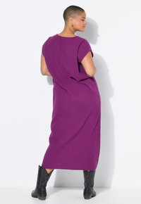 Vestido midi púrpura de una tela texturizada, con mangas cortas, un corte holgado y combinado con botas vaqueras negras.