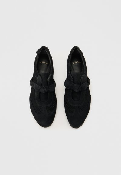 Ζευγάρι γυναικείων μοκασίνι από μαύρο σουέτ με λεπτομέρεια κόμπου στο πάνω μέρος και διάτρητο σχέδιο, με την επωνυμία Birman στο εσωτερικό.