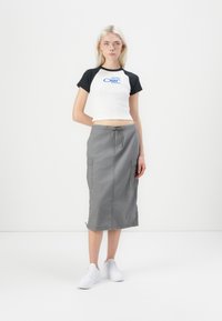 Vit kortärmad t-shirt med svarta ärmar, prydd med "Obey"-logotyp. Grå knälång cargokjol med dragsko och fickor. Vita sneakers.