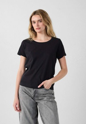 Zwarte kortebloes met korte mouwen van zacht materiaal, met een ronde halslijn en een comfortabele pasvorm, gecombineerd met lichtgrijze wijde broek.