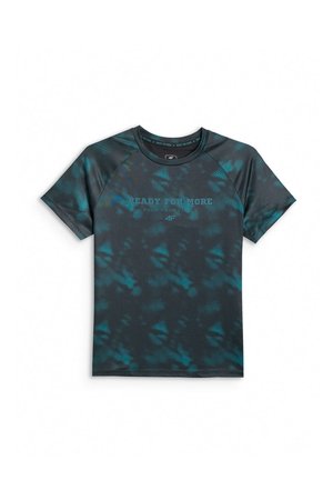 Uśmiechnięte dziecko stoi, ubrane w ciemnoniebieski t-shirt tie-dye z napisem oraz turkusowe spodnie, czarne trampki i opaskę na włosy na jednolitym szarym tle.