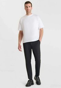 Witte T-shirt met korte mouwen gecombineerd met nauwsluitende zwarte broek. Het T-shirt is gemaakt van gladde stof; de broek heeft een subtiele textuur en een smalle snit.