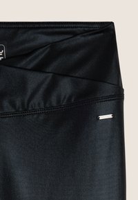 Leggings deportivos negros con una textura suave, diseño frontal cruzado y una pequeña etiqueta de logo plateada en el dobladillo.