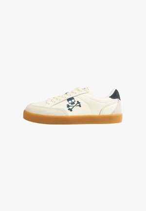 Weißes Wildledersneaker mit brauner Gummisohle, auf der Seite mit einem marineblauen Totenkopf- und Kreuzbonesymbol versehen, und einem schwarzen Akzent an der Ferse.