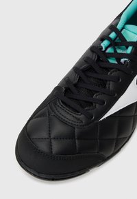 Zapatilla deportiva negra con un acabado de piel acolchada, cordones negros y acentos turquesas en el forro interior y en la marca.