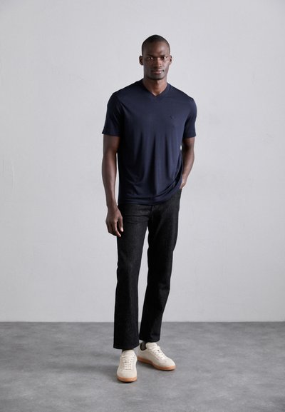Navy V-neck t-shirt with short sleeves, paired with dark denim jeans and beige sneakers. Focus on materials and simple design.