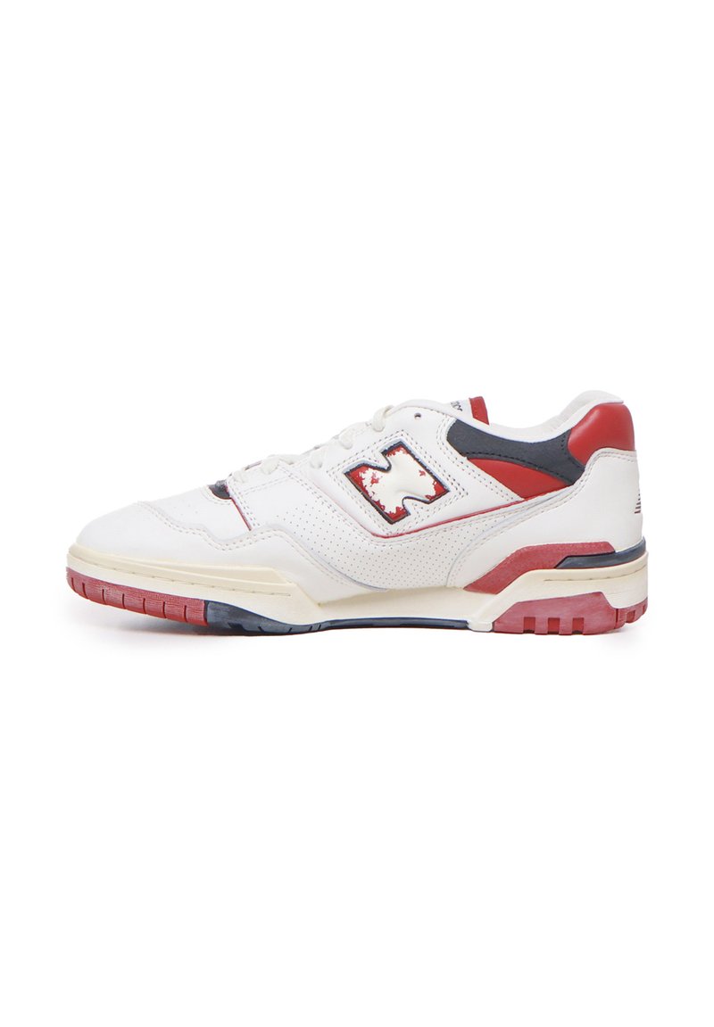 Zapatilla deportiva blanca con cuero perforado, acentos en rojo y azul marino, cuello acolchado y una suela de goma texturizada con un diseño multicolor.