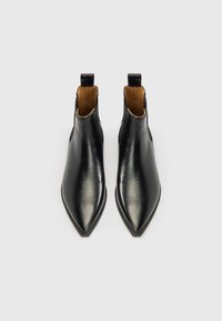 Cizme negre din piele până la gleznă, cu vârf ascuțit și decupaje laterale, având o textură netedă și căptușeală contrastantă de culoare cămilă.