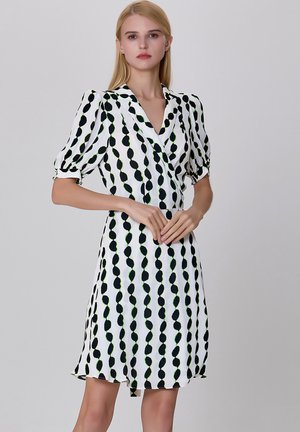 Robe blanche avec des motifs de feuilles noires et vertes. Elle présente des manches bouffantes, un décolleté en V et une jupe fluide. Texture douce.