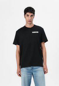 Juodas medvilninis marškinėlis su apvaliu kaklu ir trumpomis rankovėmis. Priekyje kairėje krūtinės pusėje yra balti užrašai "CALVIN KLEIN". Pritaikytas laisvam stiliui.