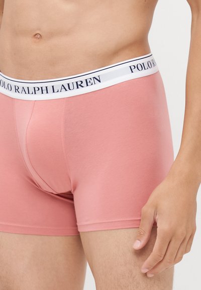 Roza bombažna bokserica z belim pasom, na katerem je mornarsko modro besedilo "POLO RALPH LAUREN". Ima gladko teksturo in prilegajoč dizajn.