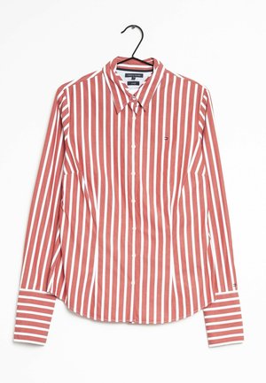 Langärmliges Hemd mit roten und weißen vertikalen Streifen, Knopfleiste und Kragen, aufgehängt an einem schwarzen Bügel vor weißem Hintergrund.