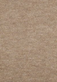 Beige gebreide textiel met een fijn geribbeld patroon, dat een zachte textuur en een consistente kleur in het hele materiaal laat zien. Geschikt voor kleding of accessoires.