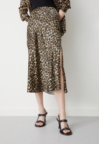 Sukně s leopardím potiskem z lehkého materiálu se bočním rozparkem. Černé sandály na vysokém podpatku s přezkou doplňují celý outfit.