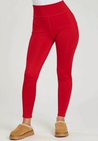 Leggings rouges taille haute en tissu extensible avec une texture lisse, présentant un design ajusté et sans motifs ni accents visibles.