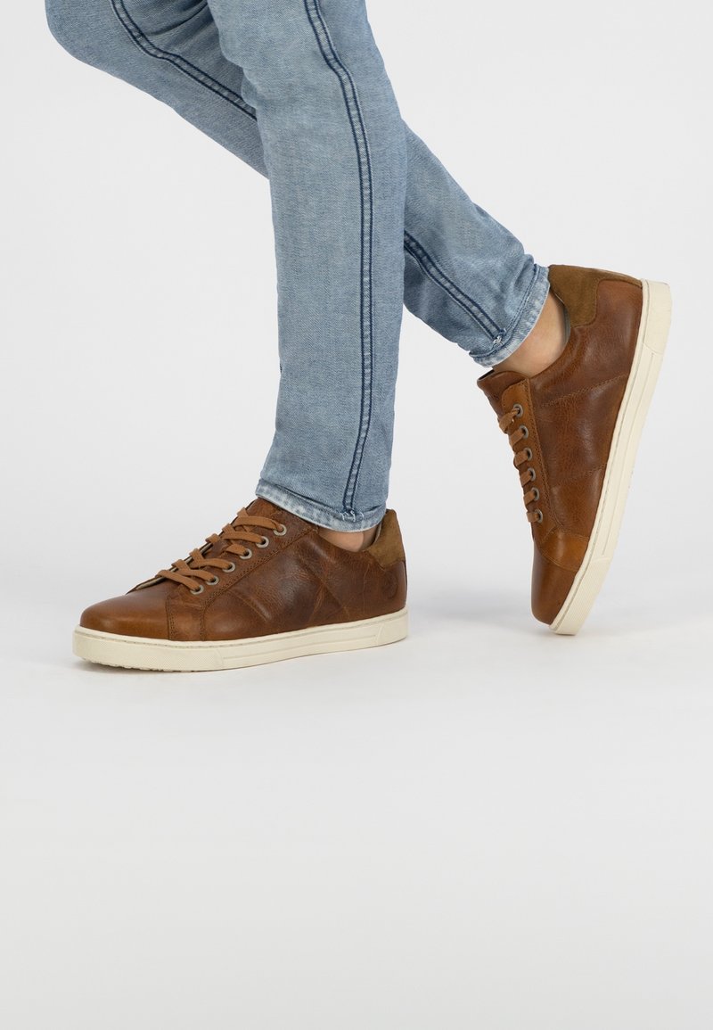 Bruna lädersneakers med beige gummisula, med snörning, texturerade detaljer och en minimalistisk design. Matchas med ljusblå jeans.