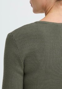 Ribbad långärmad topp i olivgrön, med ett texturerat stickat mönster och rundad nacke. Bakifrån framhävs tygets elasticitet.