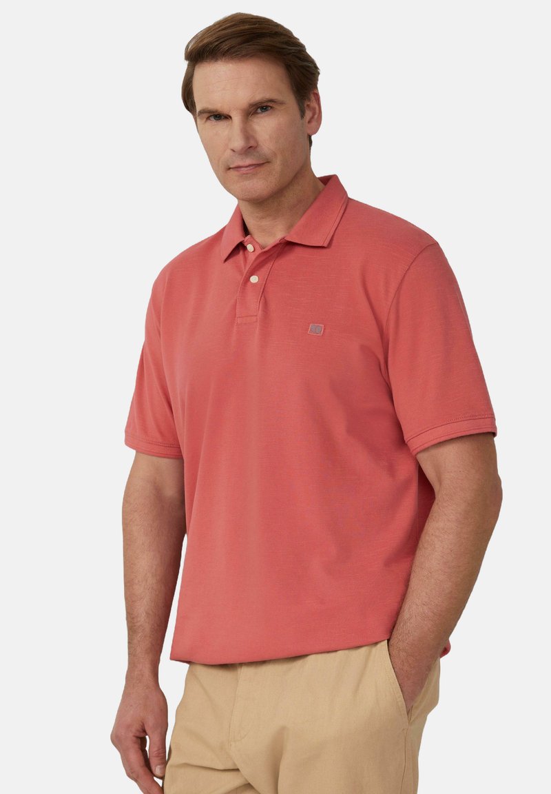 Koszulka polo w kolorze koralowym, z krótkimi rękawami oraz kołnierzykiem, z trzema guzikami przy szyi i dyskretnym logo na piersi.