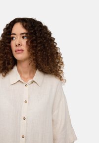 Leinenhemd in hellem Beige mit Relaxed Fit, kurzen Ärmeln und einer durchgehenden Knopfleiste, die einen runden Kragen und Kunststoffknöpfe umfasst.