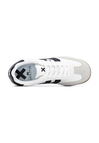 Zapatilla blanca con detalles en gamuza gris, rayas negras y una suela de goma texturizada. Presenta cordones y una plantilla acolchada con la marca.