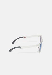 Sonnenbrille mit klarem Kunststoffrahmen und lila verspiegelten Gläsern. Graue Gummibeschläge an den Bügeln und rotes Logodetail an der Seite.