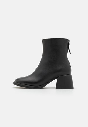 Bottines noires à finition en cuir lisse, à bout rond et à talon épais. Dotées d'une fermeture éclair sur le côté pour un enfilage facile.