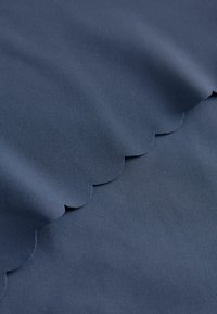 Tkanina w kolorze granatowym o gładkiej teksturze, z falbaniastym brzegiem. Materiał wydaje się trwały, odpowiedni do różnych zastosowań.