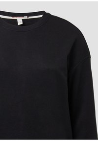 Schwarzer Rundhalsausschnitt-Pullover mit langen Ärmeln und einem kleinen weißen Etikett nahe dem Ausschnitt vor einem hellgrauen Hintergrund.