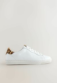 Baskets en cuir blanc avec lacets et semelle blancs, présentant un détail imprimé léopard sur la languette du talon, sur un fond clair uni.