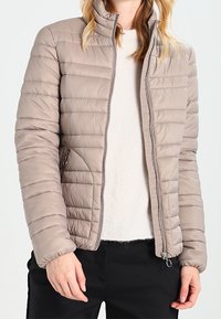 Beige gewatteerde jas met een hoge kraag, ritssluiting aan de voorkant en zijzakken. Glad textuur en licht aangesloten ontwerp, geschikt voor het laagjes dragen.