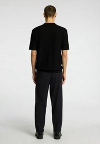 Maglietta nera a maniche corte in maglia con un motivo testurizzato, abbinata a pantaloni neri e scarpe nere, vista da dietro.