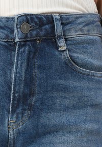 Denimjeans i en medelvattnig tvätt med en klassisk femficksdesign, med en metallknapp och orangea stickningar längs sömmarna.