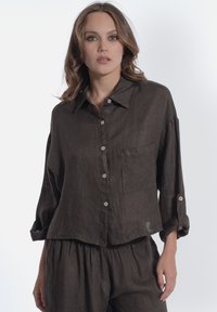 Camicia button-up in lino marrone con tasca, maniche arrotolate e vestibilità rilassata. Texture liscia, design minimalista e colore neutro.